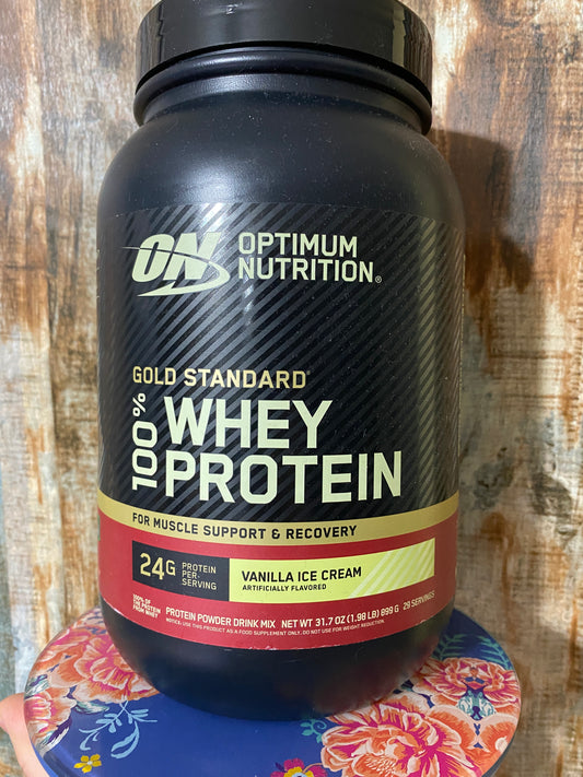 Optimum Nutrition whey protein supplement bottle on a wooden surface with a colorful coaster.